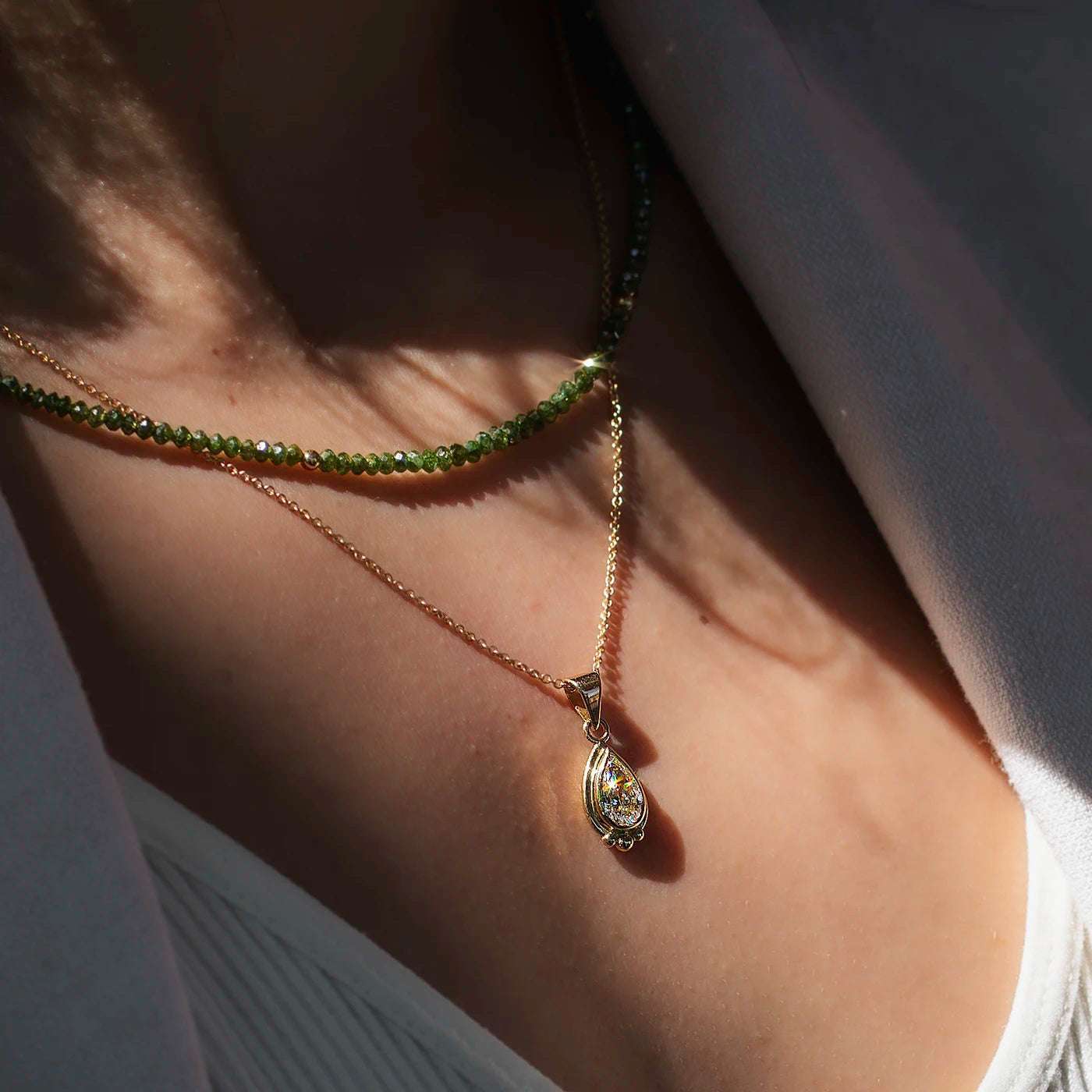 Anhaenger grosser Diamant Tropfen 1.0ct in Gelbgold Fan Modelhals mit gruener Diamantkette, Diamanttropfen funkelt im Sonnenlicht nah