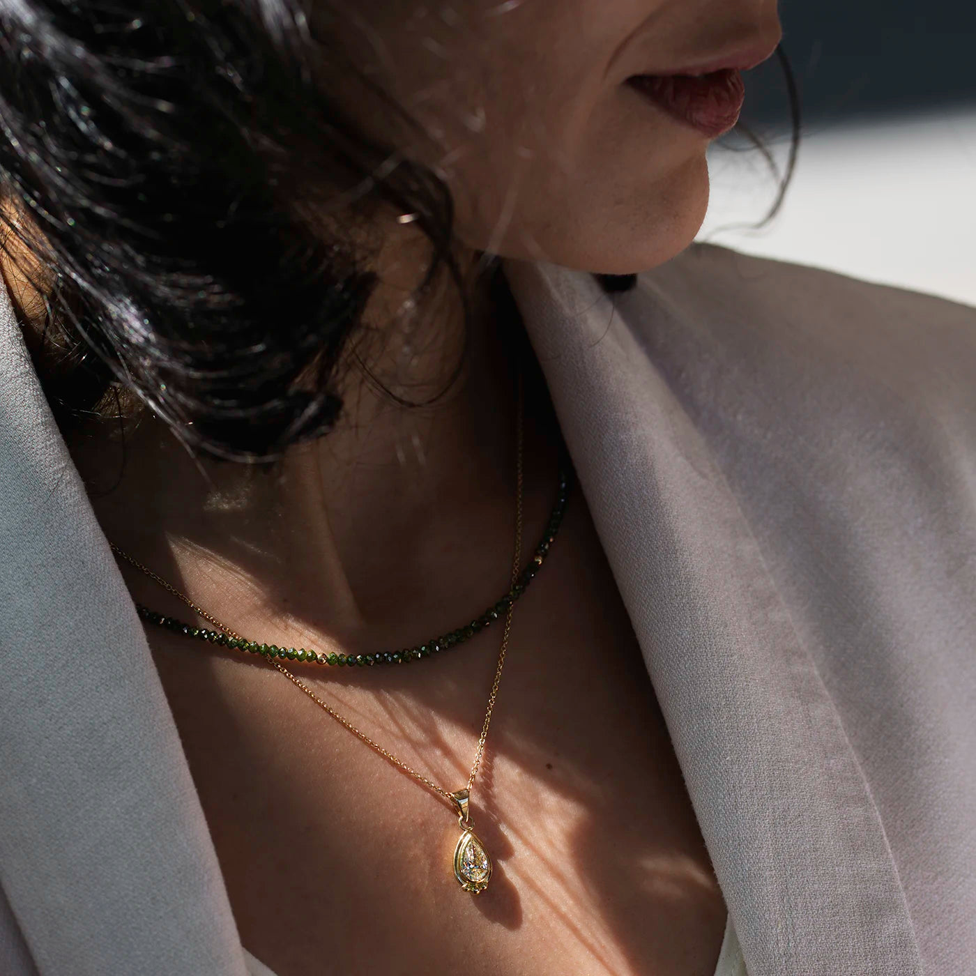 Anhaenger grosser Diamant Tropfen 1.0ct in Gelbgold Fan Modelhals mit gruener Diamantkette, Diamanttropfen funkelt im Sonnenlicht nah Model schaut weg