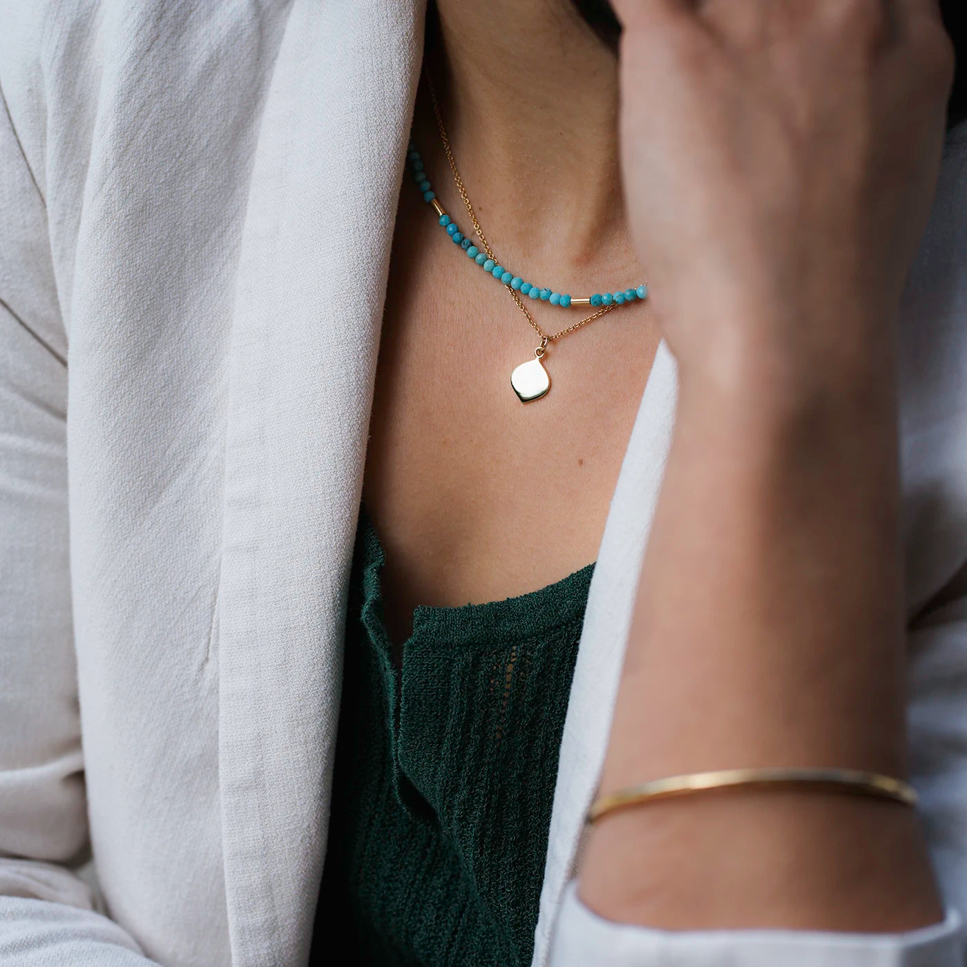 Kette Josefine Gravurplättchen in Logoform 10mm x 15mm Gelbgold an Modelhals mit gruenem Oberteil closeup schraeg von rechts