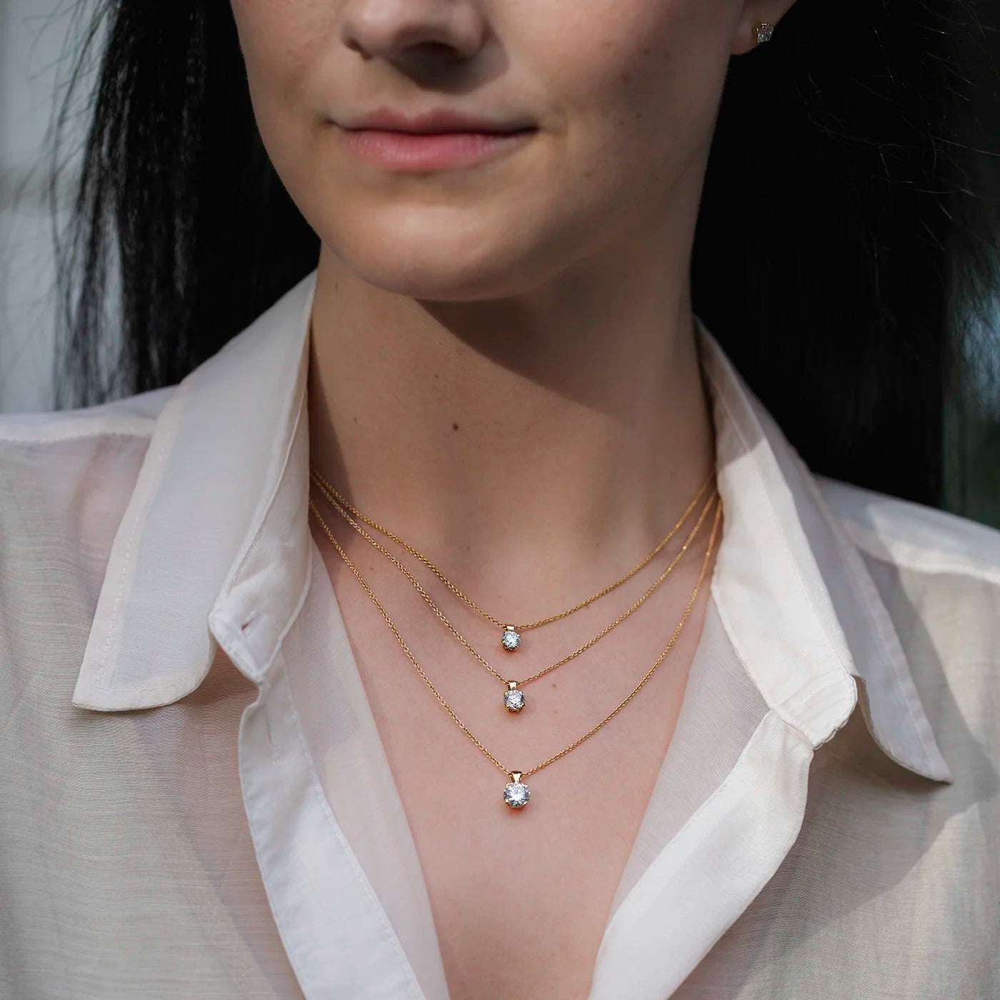 Anhaenger Petite Fleur Layering mit 0.50ct 0.80ct und 1.20ct Brillanten in Gelbgold an modelhals mit weissem Oberteil draussen Model schaut links halbnah frontal