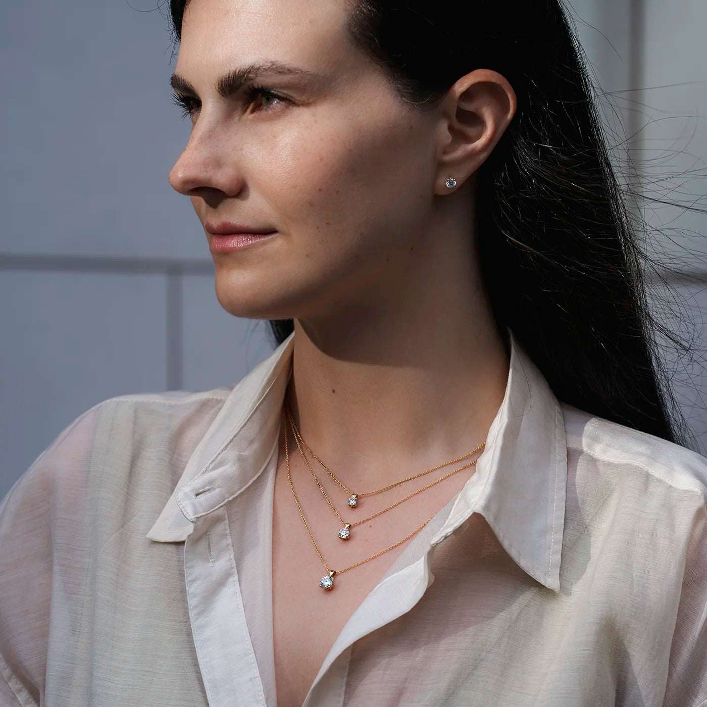 Anhaenger Petite Fleur Layering mit 0.50ct 0.80ct und 1.20ct Brillanten in Gelbgold an modelhals mit weissem Oberteil draussen Model schaut links halbnah