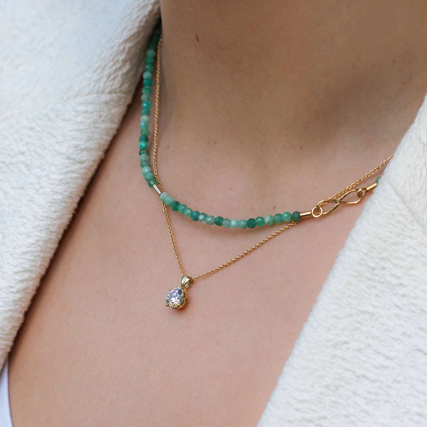 Anhaenger Petite Fleur mit 1.20ct Brillant in Gelbgold an Model mit weisser Stoff Jacke closeup mit Edelsteinkette Smaragd Gelbgold