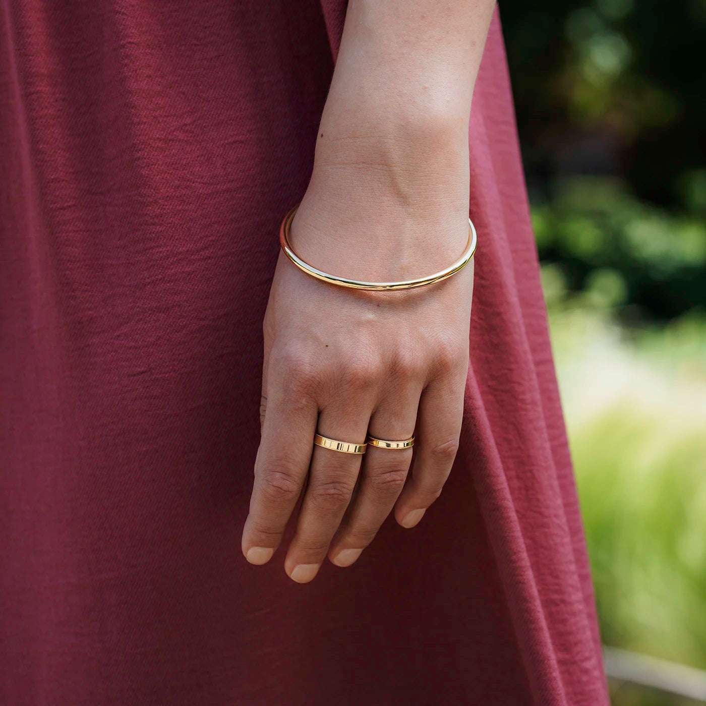 Klassischer runder Armreif mit 4mm Materialstaerke ohne Verschluss an Modelarm auf Handgelenk Hand zeigt nach unten vor rotem Kleid