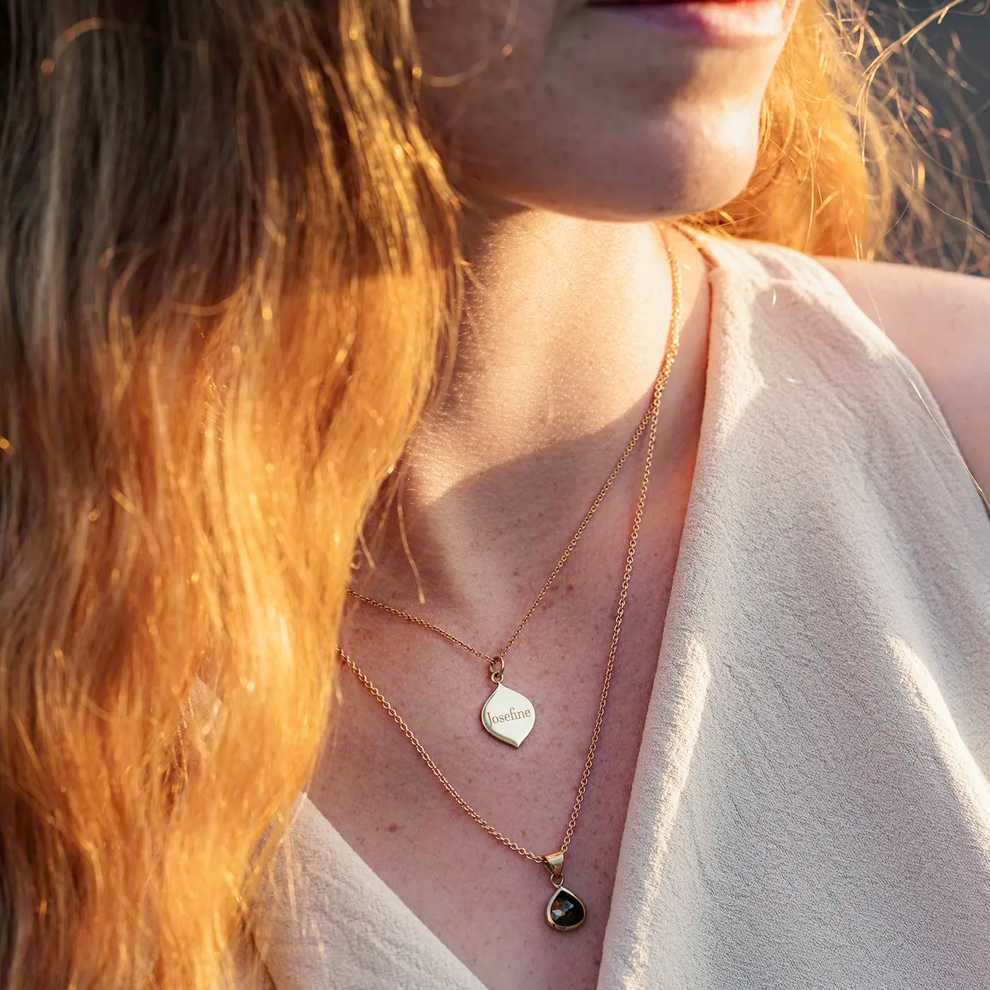 Gravurplaettchen aus Gelbgold in Josefine Logoform in der Grösse 13x21mm an Modelhals nah bei Sonnenuntergang mit Gravur Josefine