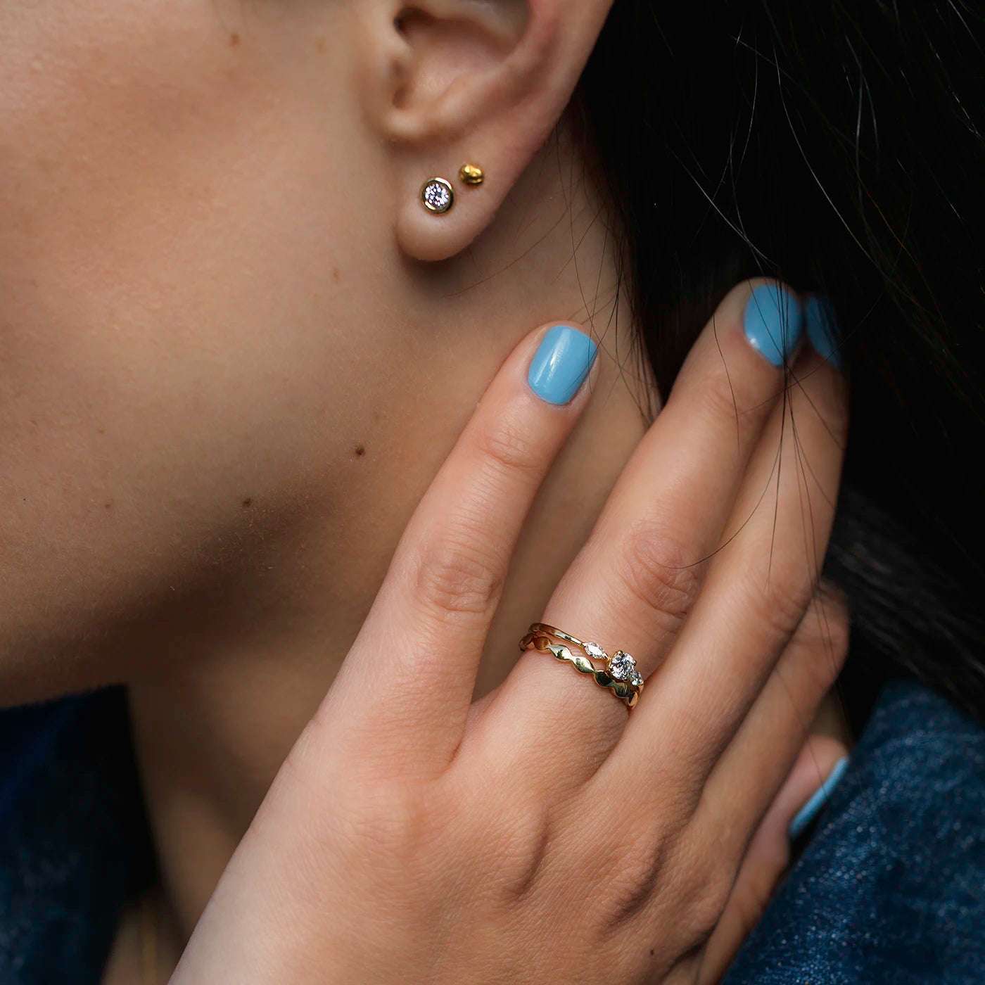 Ein Ohrstecker Balance mit einem 0,15 ct Brillanten in Gelbgold an Modelohr mit Hand im Vordergrund mit Diamantring