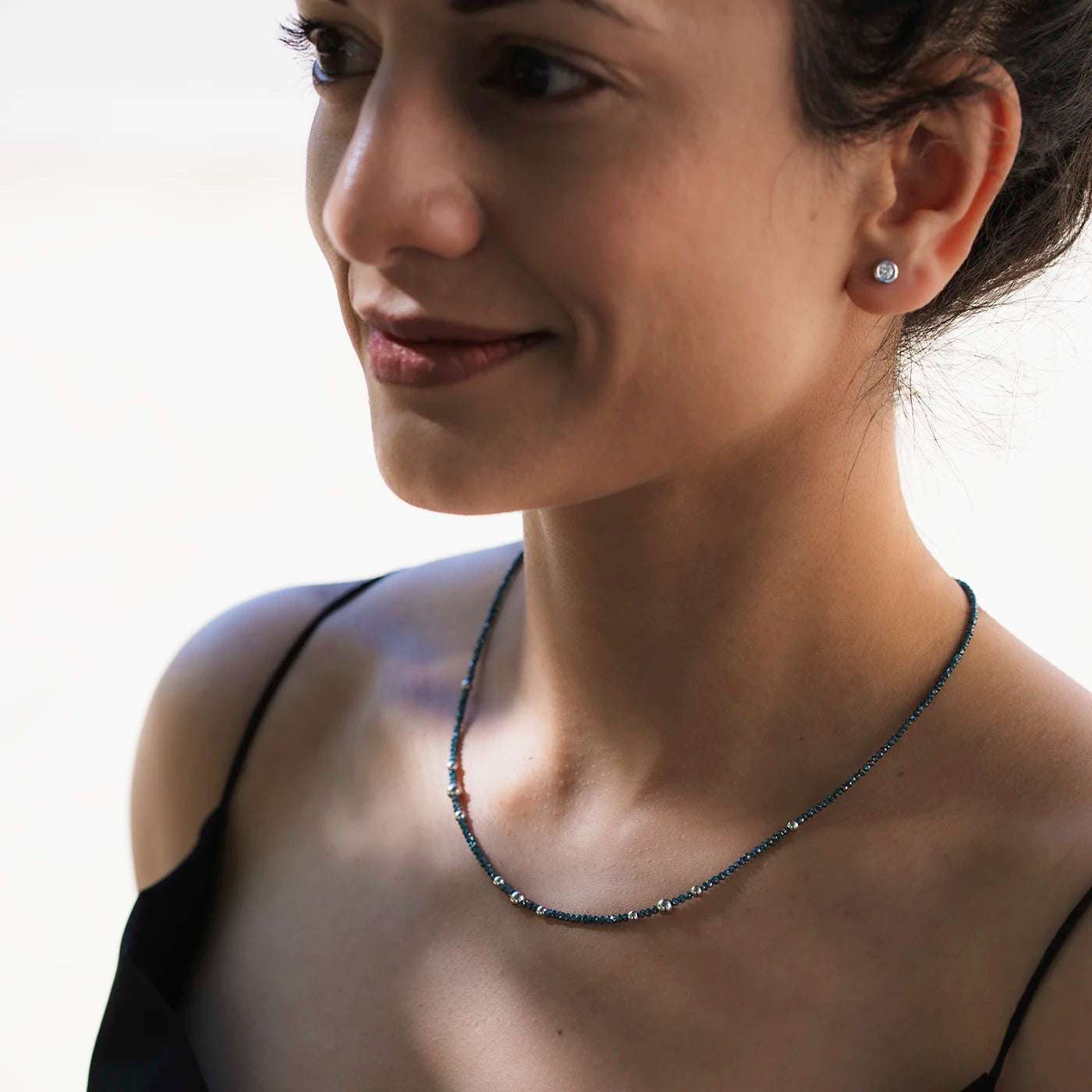 Ein Balance Ohrstecker mit einem 0.15ct Brillanten aus Platin an weiblichem Model mit DIamantkette am Hals