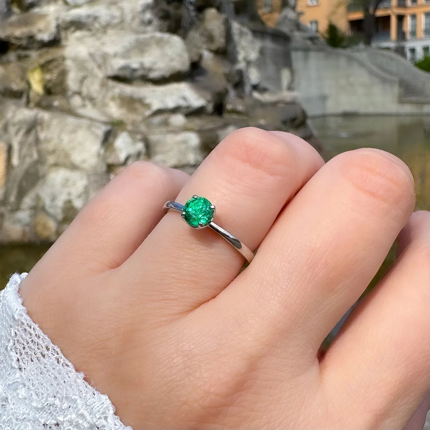 Petite Fleur Solitär Ring aus 950er Platin mit grünem Smaragd am Finger getragen vor Brunnen in Berlin Wilmersdorf halbnah