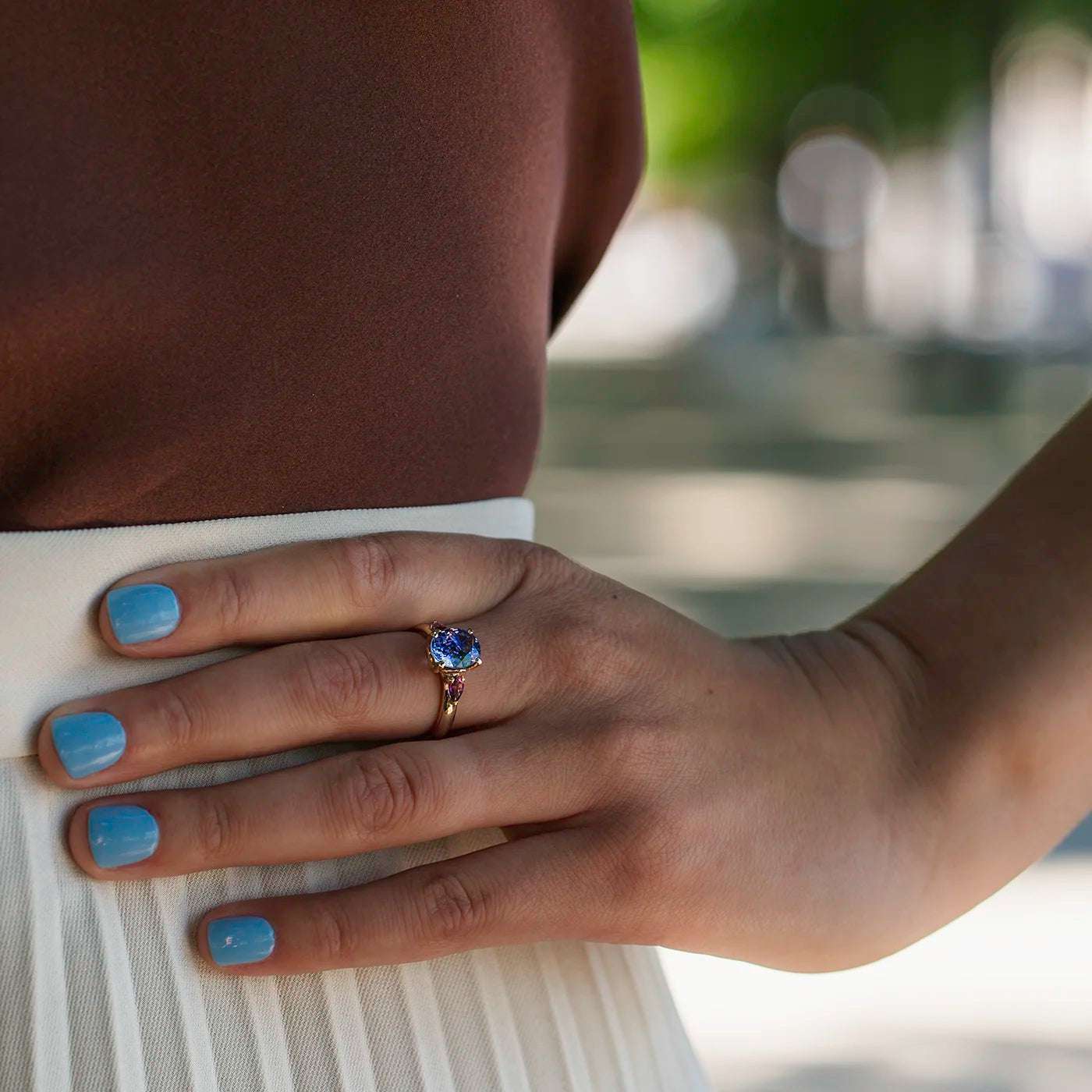 Ring Fleur Unikat blauer Tansanit und zwei magentarote Granate Rosegold im floralem Design an Modelhand auf Mittelfinger Hand auf Huefte