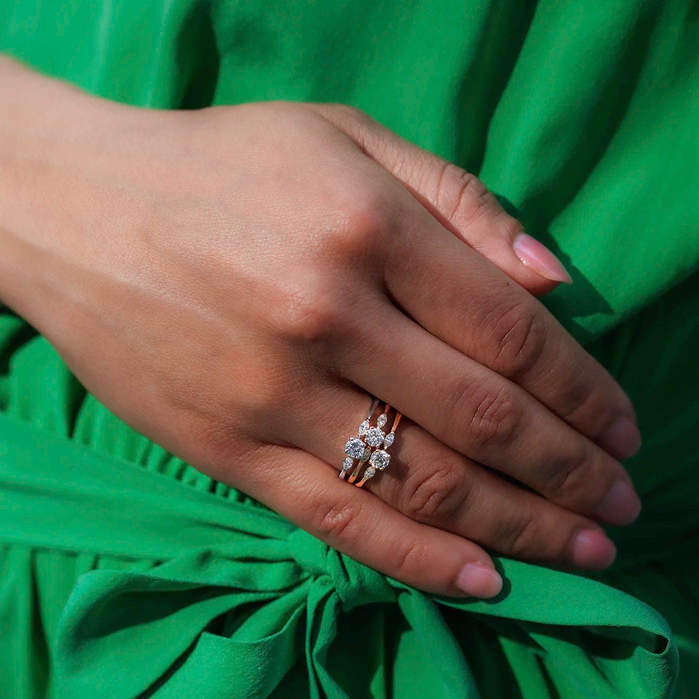 Alle 3 Varianten vom Ring Petite Fleur 0,25 ct Rose Gelbgold und Platin als Stacked Ringe auf dem Ringfinger vor gruenem Kleid closeup