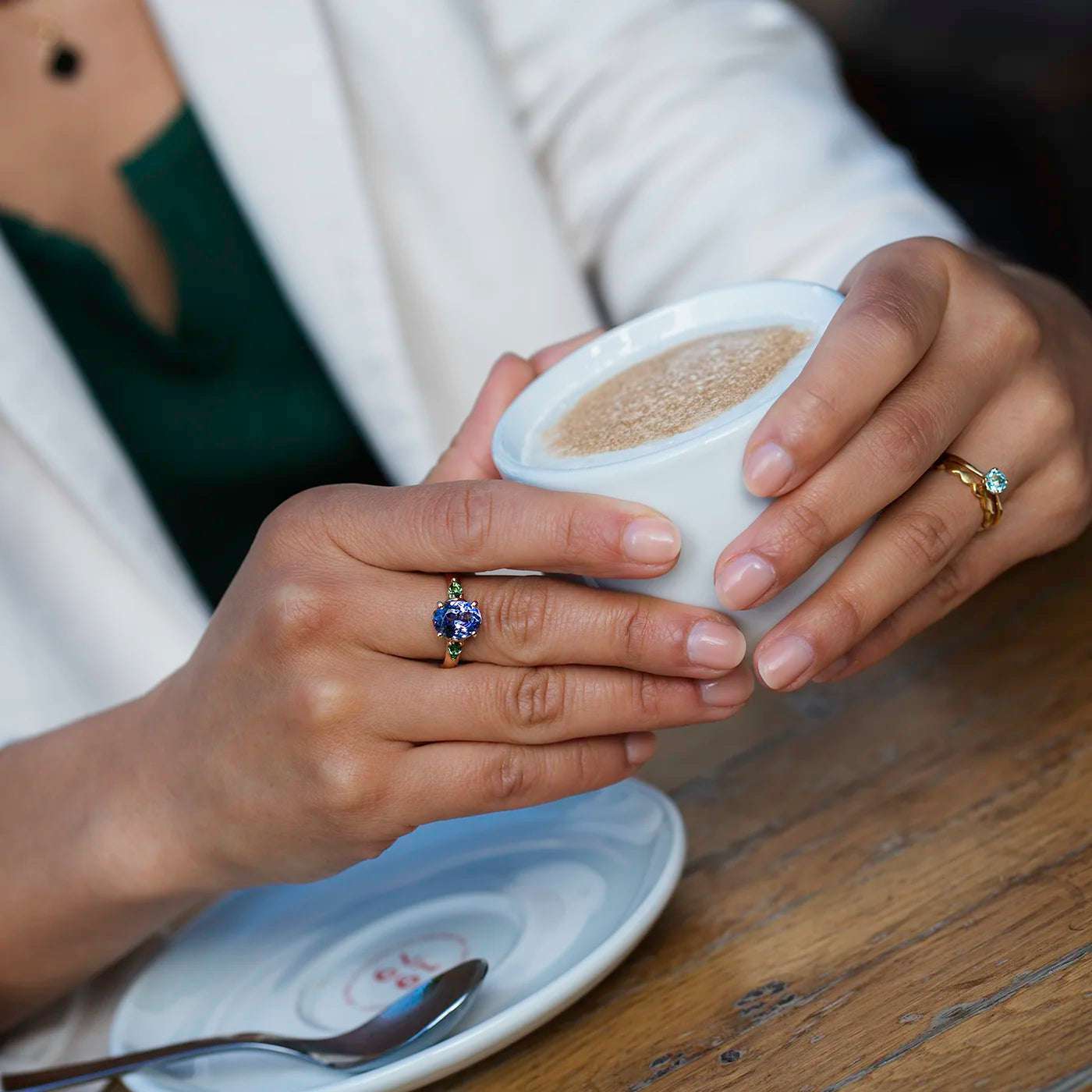 Ring Fleur Unikat blauer Tansanit und zwei gruene Turmaline Gelbgold im floralem Design an Modelhand haelt Kaffeetasse