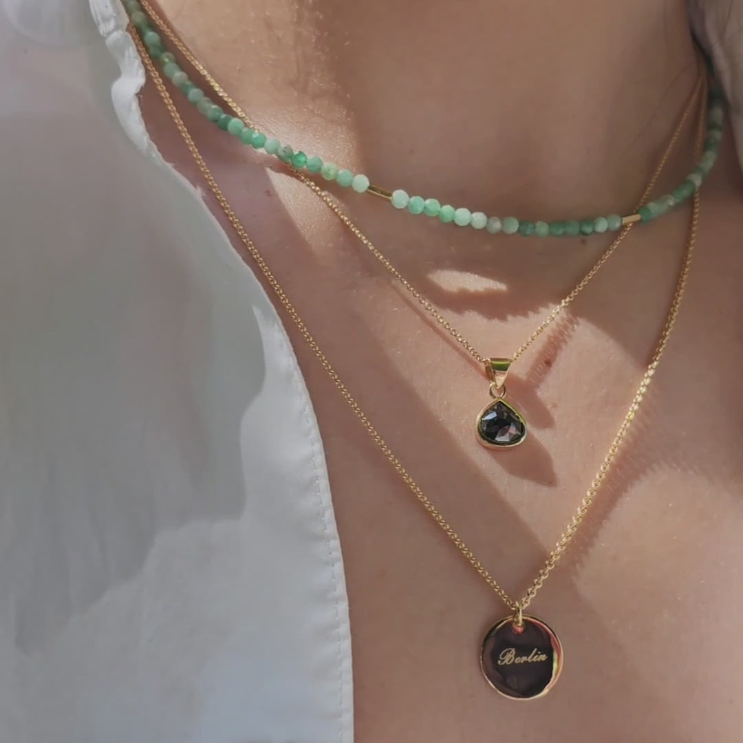weibliches Model traegt Edelsteinkette Smarag mit Gelbgold, Gravurplaettchen in Rund und Gelbgold und einen Anhaenger mit schwarzem Diamanten 1.50ct Gelbgold