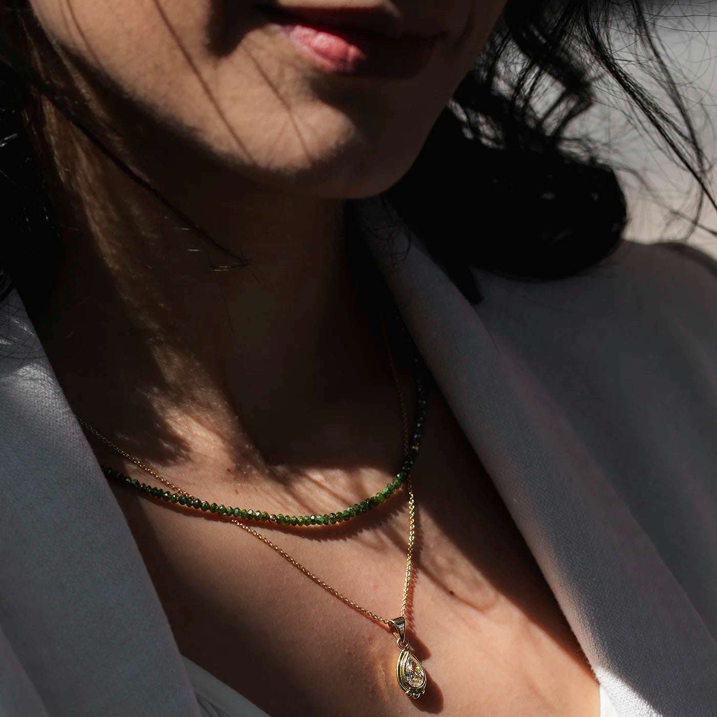 Anhaenger grosser Diamant Tropfen 1.0ct in Gelbgold Fan Modelhals mit gruener Diamantkette, Diamanttropfen funkelt im Sonnenlicht halbnah