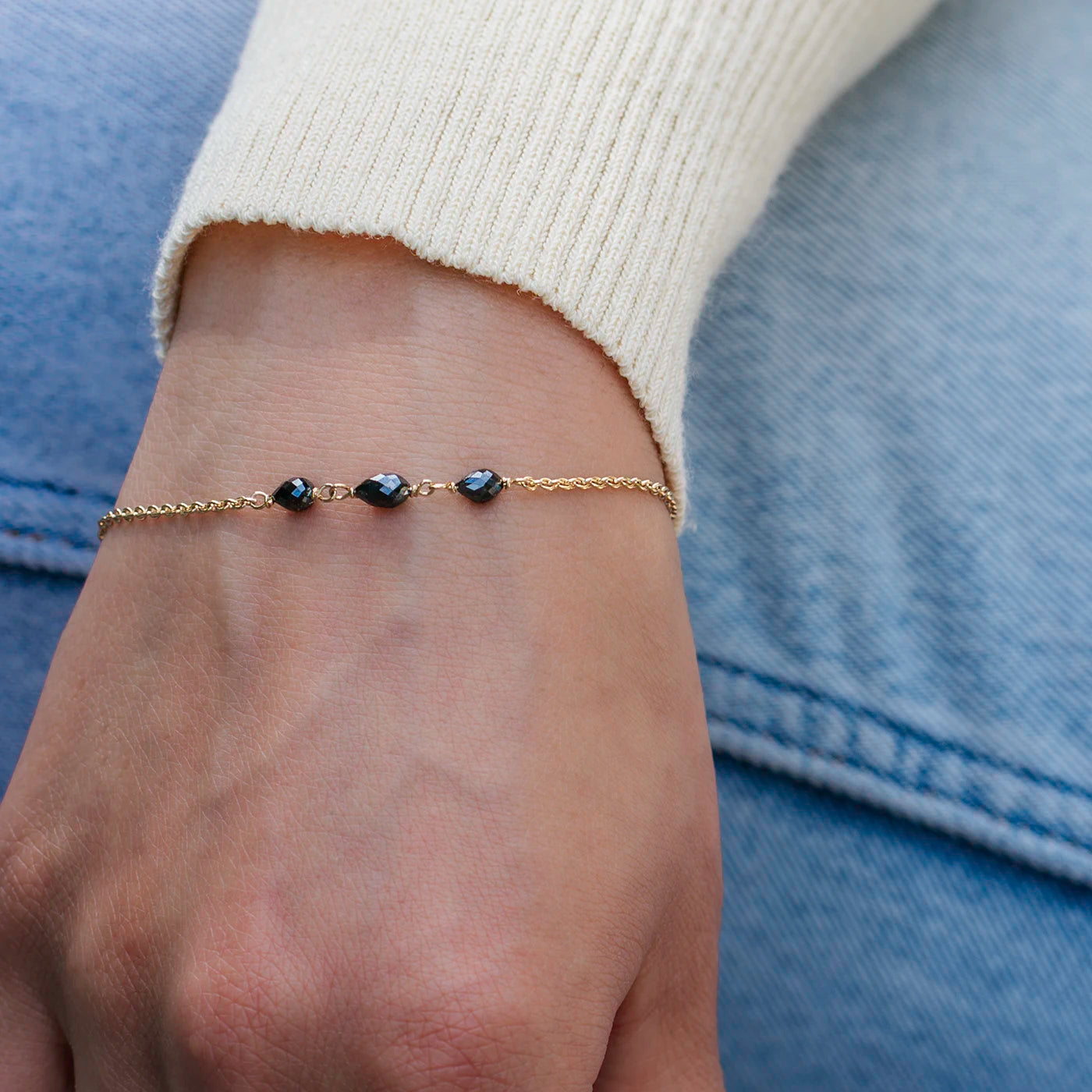 Armband aus Gelbgold mit drei schwarzen Diamanten Tropfenform an Modelarm vor blauer Jeans closeup