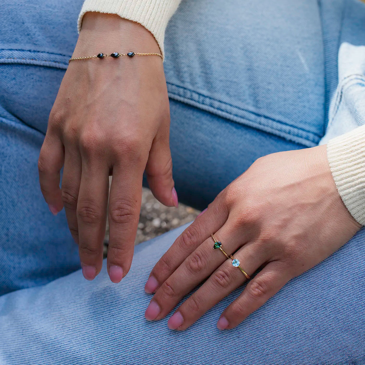 Armband aus Gelbgold mit drei schwarzen Diamanten Tropfenform an Modelarm vor blauer Jeans