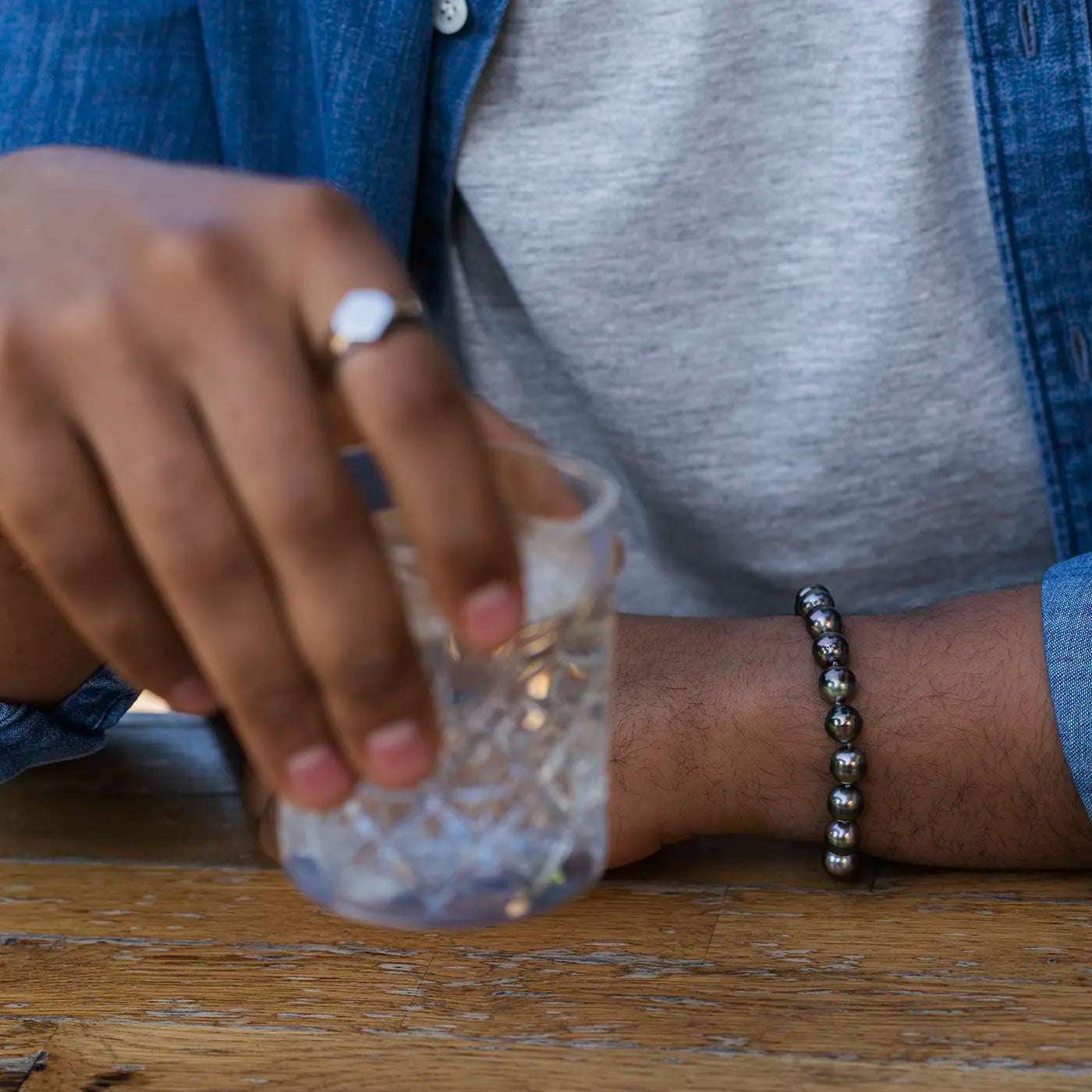 Armband aus Tahiti Perlen mit Platin Verschluss an maennlichem Modelhandgelenk Hand liegt auf Tisch