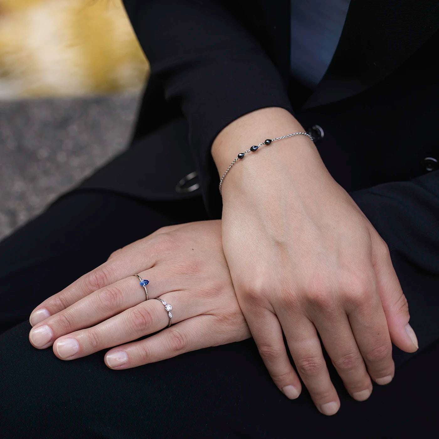 Armband aus Platin mit drei schwarzen Diamanten Tropfenform an Modelhand auf schwarzem Aermel von Blazer