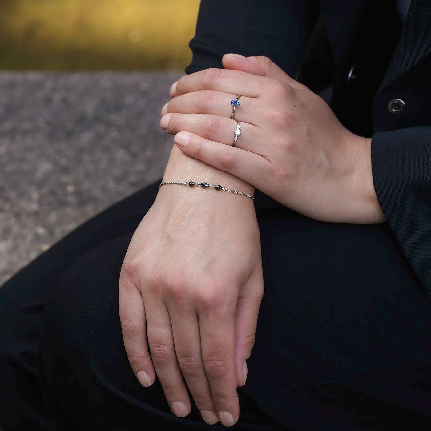 Armband aus Platin mit drei schwarzen Diamanten Tropfenform an Modelhand auf schwarzem Aermel von Blazer closeup