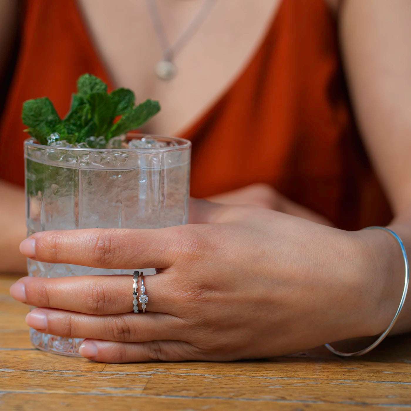 Ring Wave Platin die Ringschiene ist geschwungen wie Wellen Frontansicht an Modelhand Mittelfinger mit Zusteckring Petite Fleur in Platin Hand haelt Glas