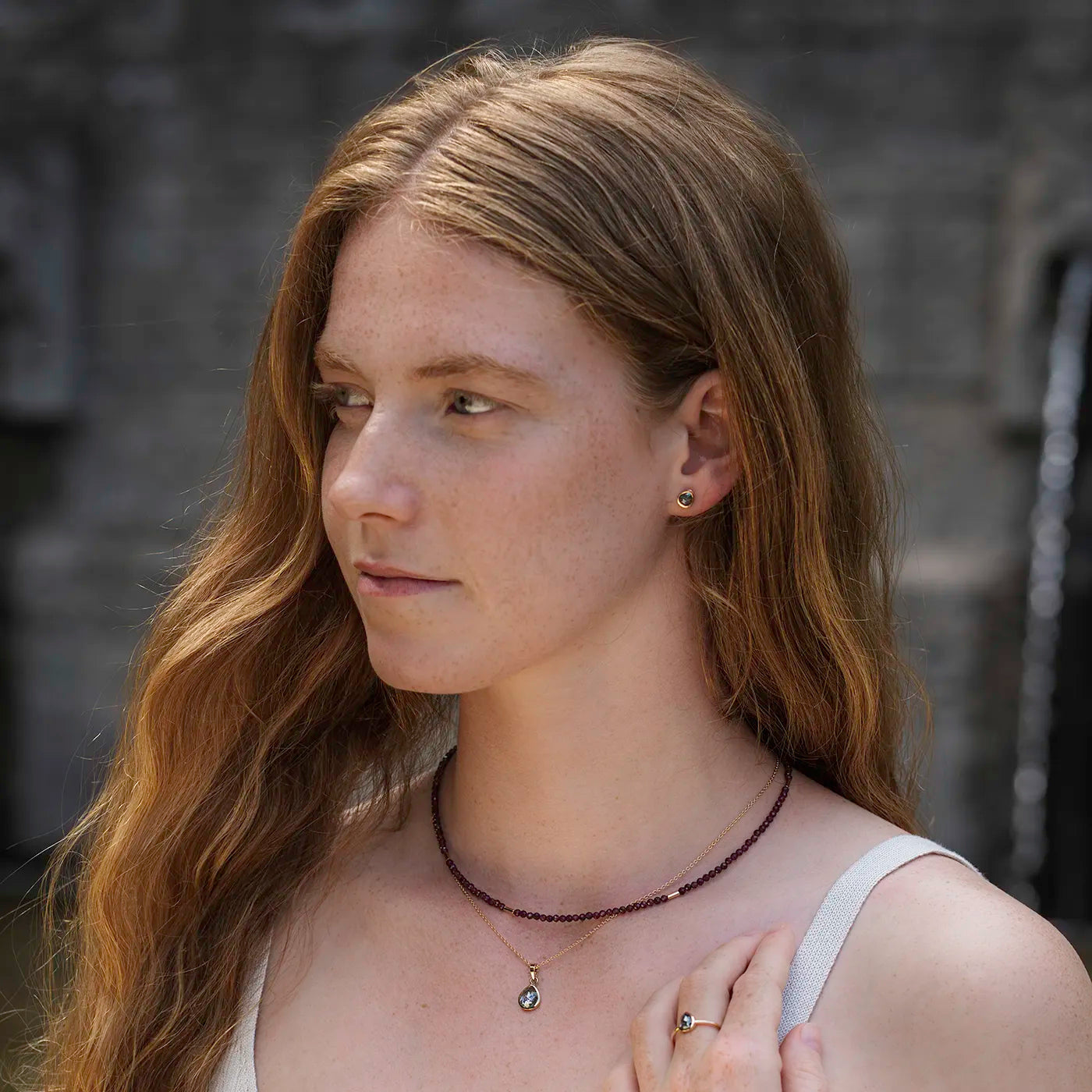 Edelsteinkette mit Granat und Rosegold Elementen an Modelhals vor Brunnen nah