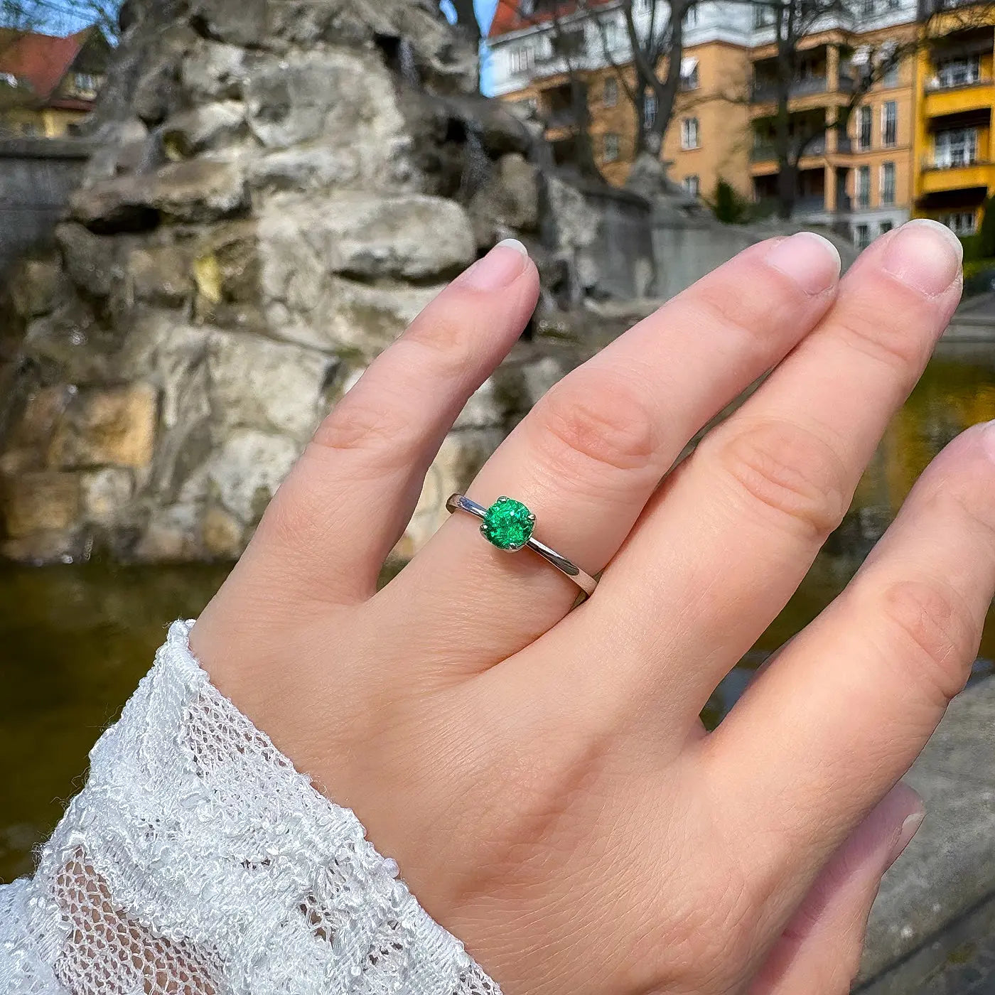 Petite Fleur Solitär Ring aus 950er Platin mit grünem Smaragd am Finger getragen vor Brunnen in Berlin Wilmersdorf