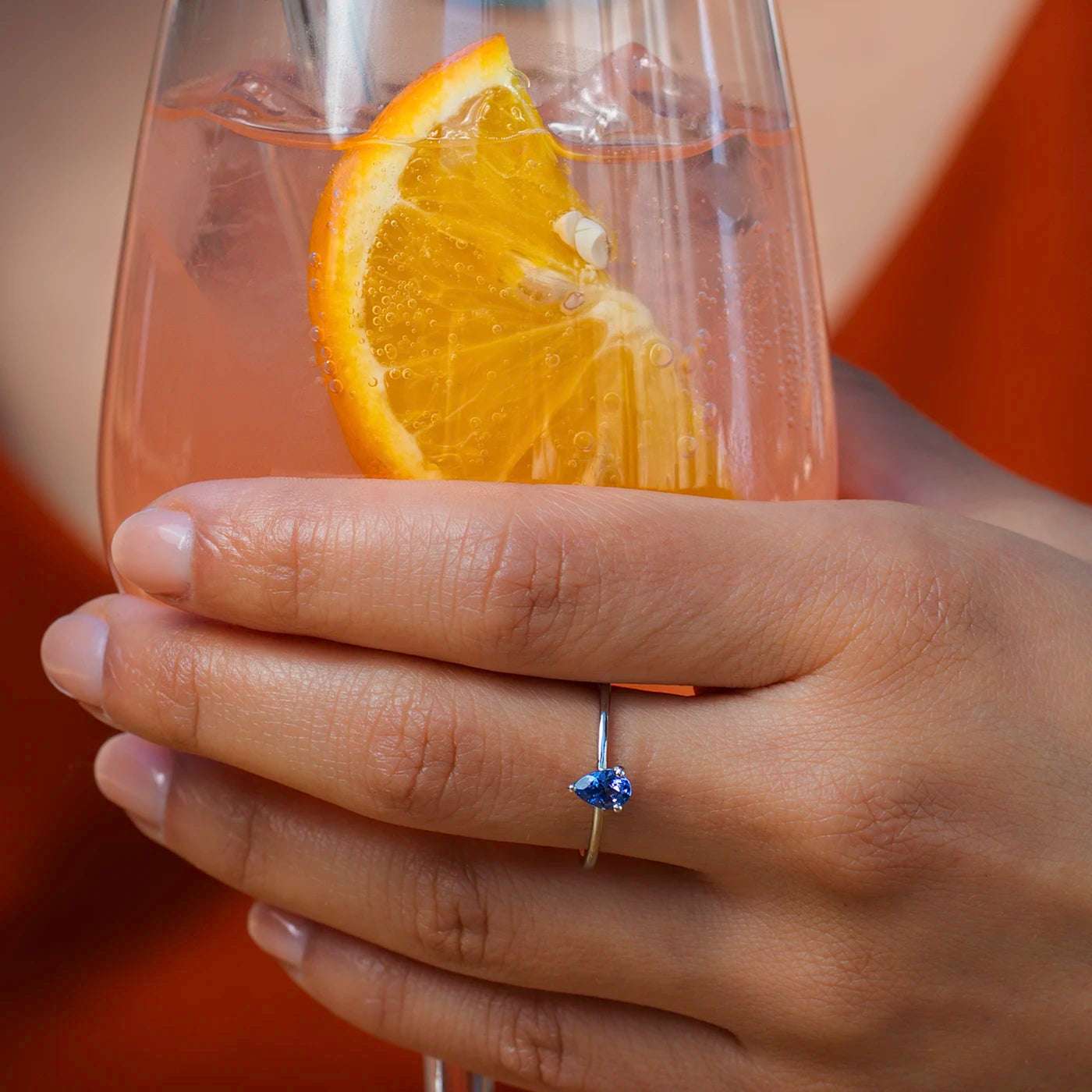 Ring Blossom ein blauer Tansanit Platin an modelhand closeup Glas in Hand mit Drink