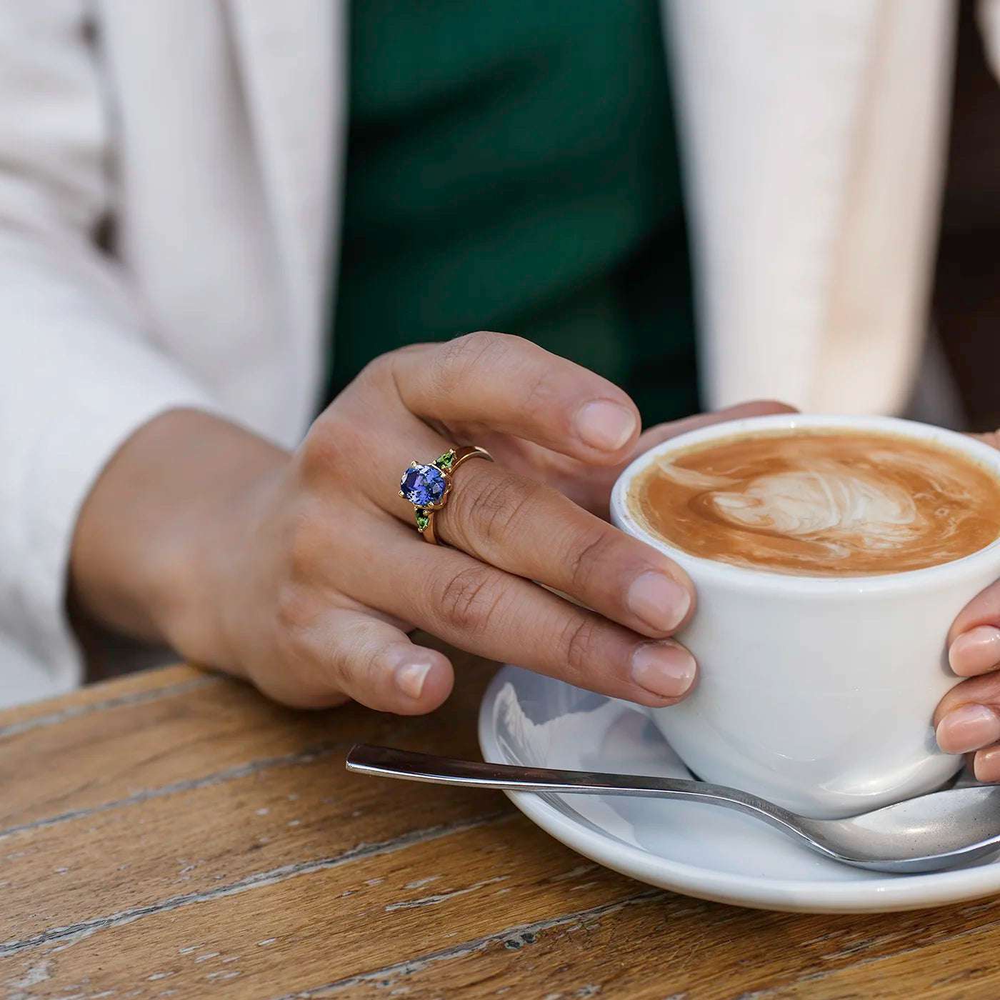 Ring Fleur Unikat blauer Tansanit und zwei gruene Turmaline Gelbgold  im floralem Design an Modelhand an Kaffeetasse