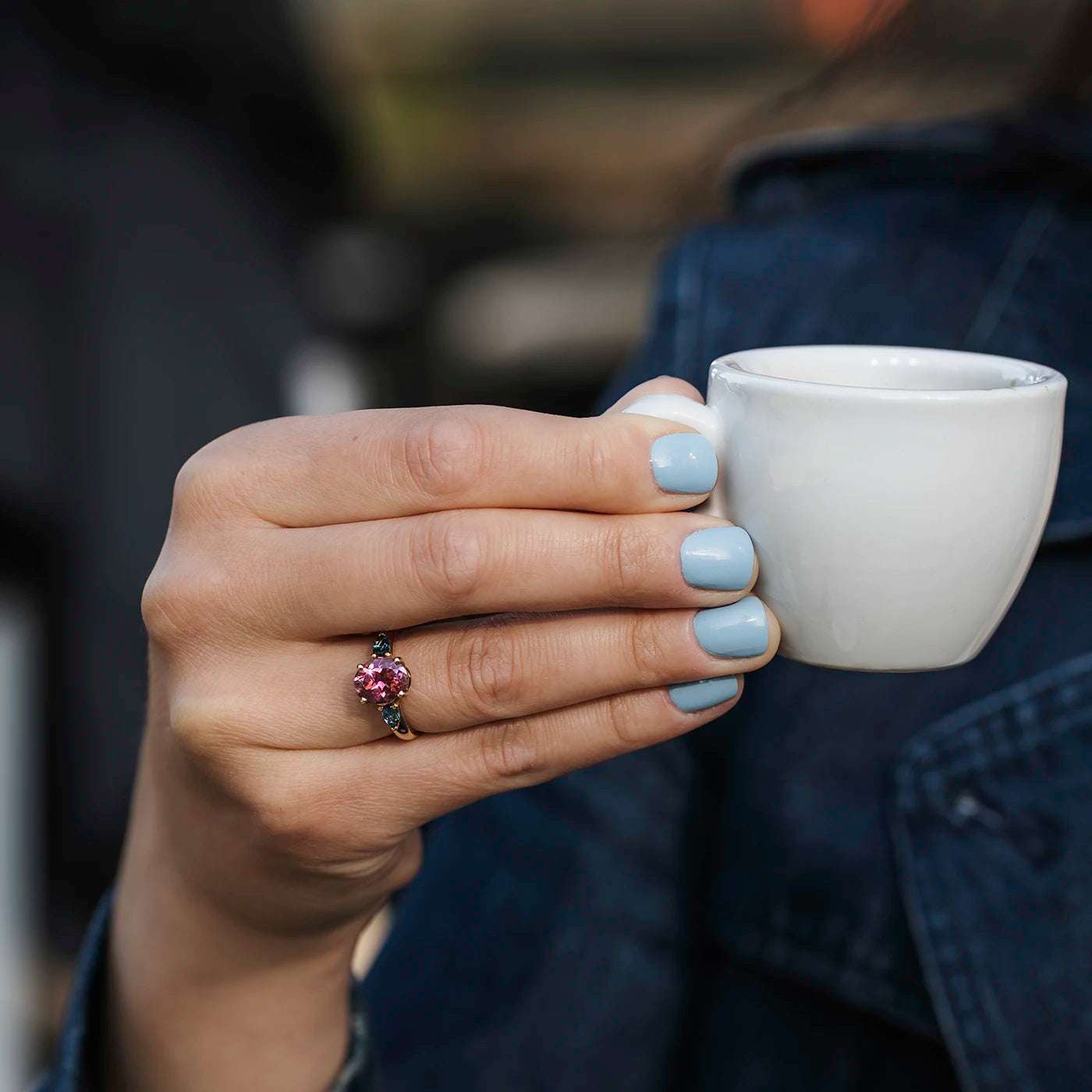 Ring Fleur Unikat roter Turmalin und zwei blaue Topas im floralem Design an Ringfinger Model Hand haelt kaffeetasse