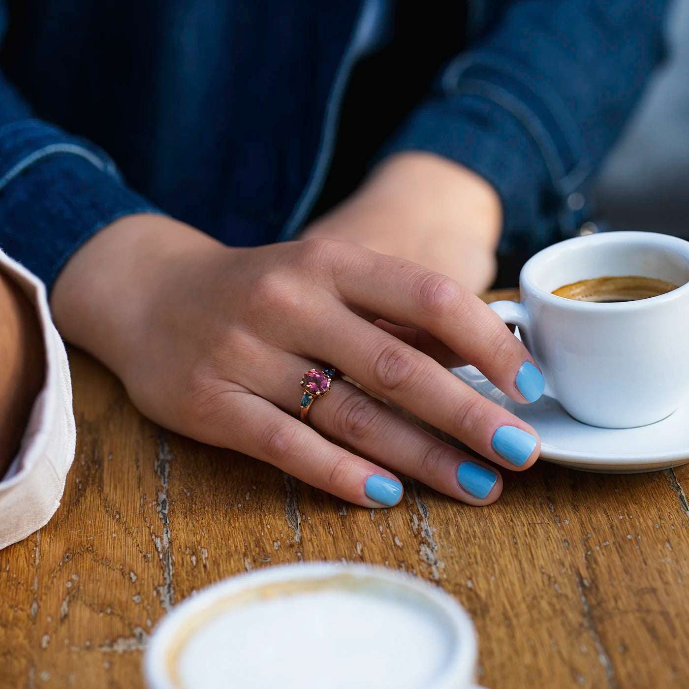 Ring Fleur Unikat roter Turmalin und zwei blaue Topas im floralem Design an Ringfinger Model Hand auf Kaffeetisch