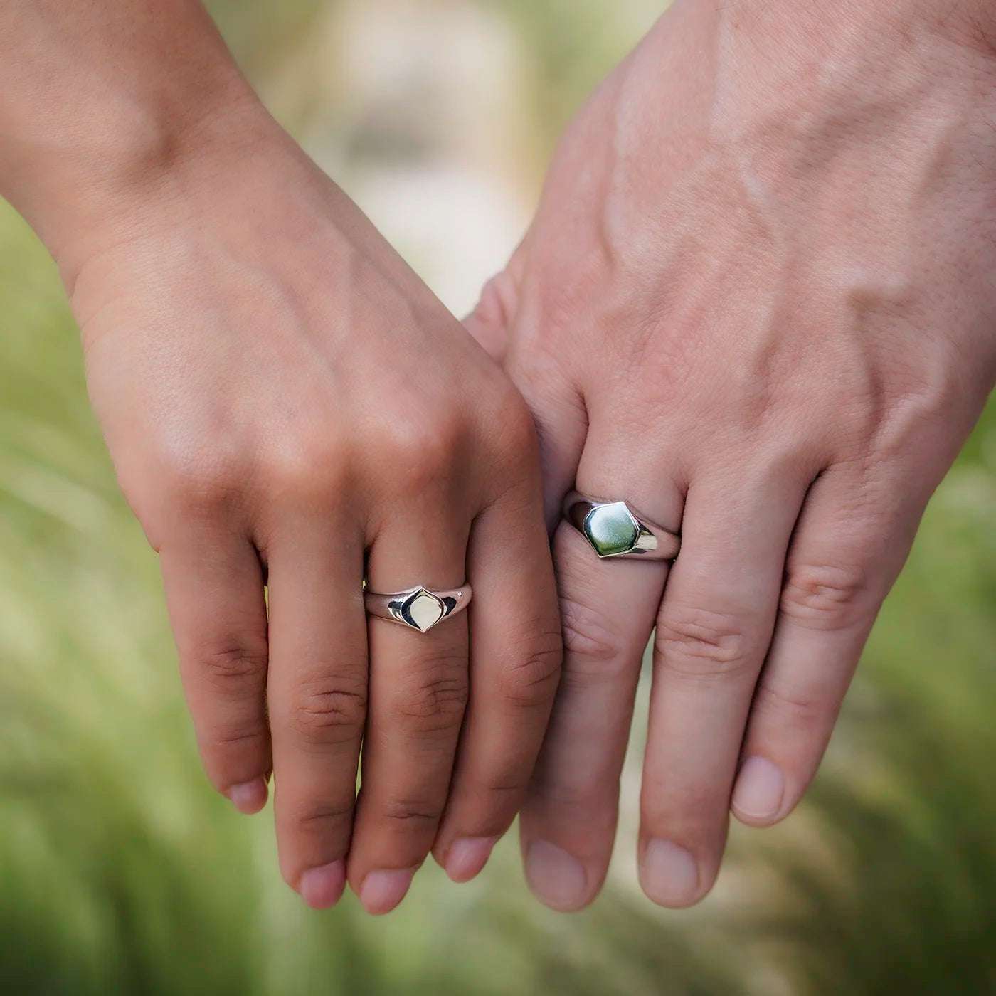 Siegelring Damen und Herrenring Platin mit grosser Flaeche in Form Josefine Logo fuer Wunschgravur Frontansicht an weiblich und maennlicher Modelhand MIttelfinger halten Haende vor gruen Closeup