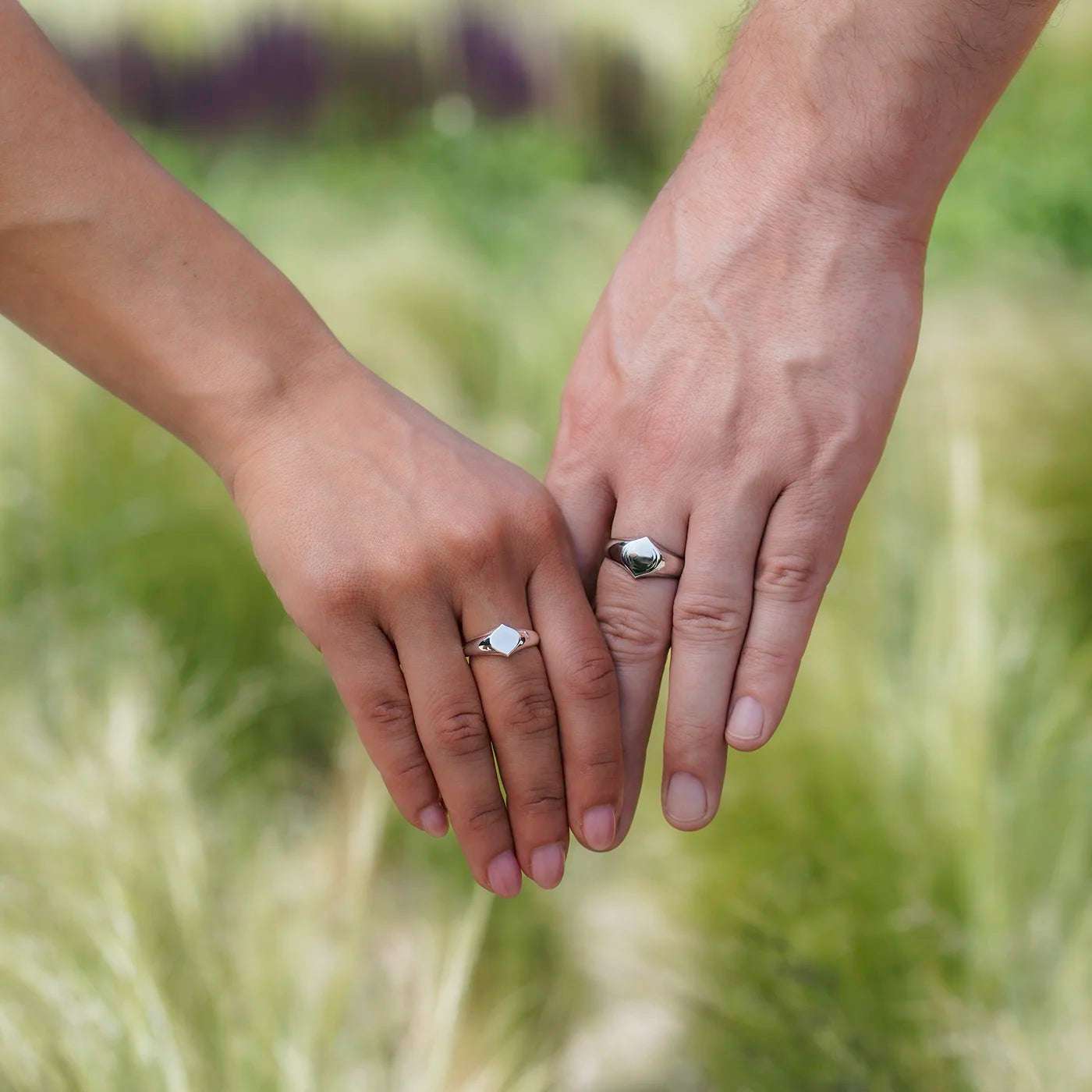 Siegelring Damen und Herrenring Platin mit grosser Flaeche in Form Josefine Logo fuer Wunschgravur Frontansicht an weiblich und maennlicher Modelhand MIttelfinger halten Haende vor gruen