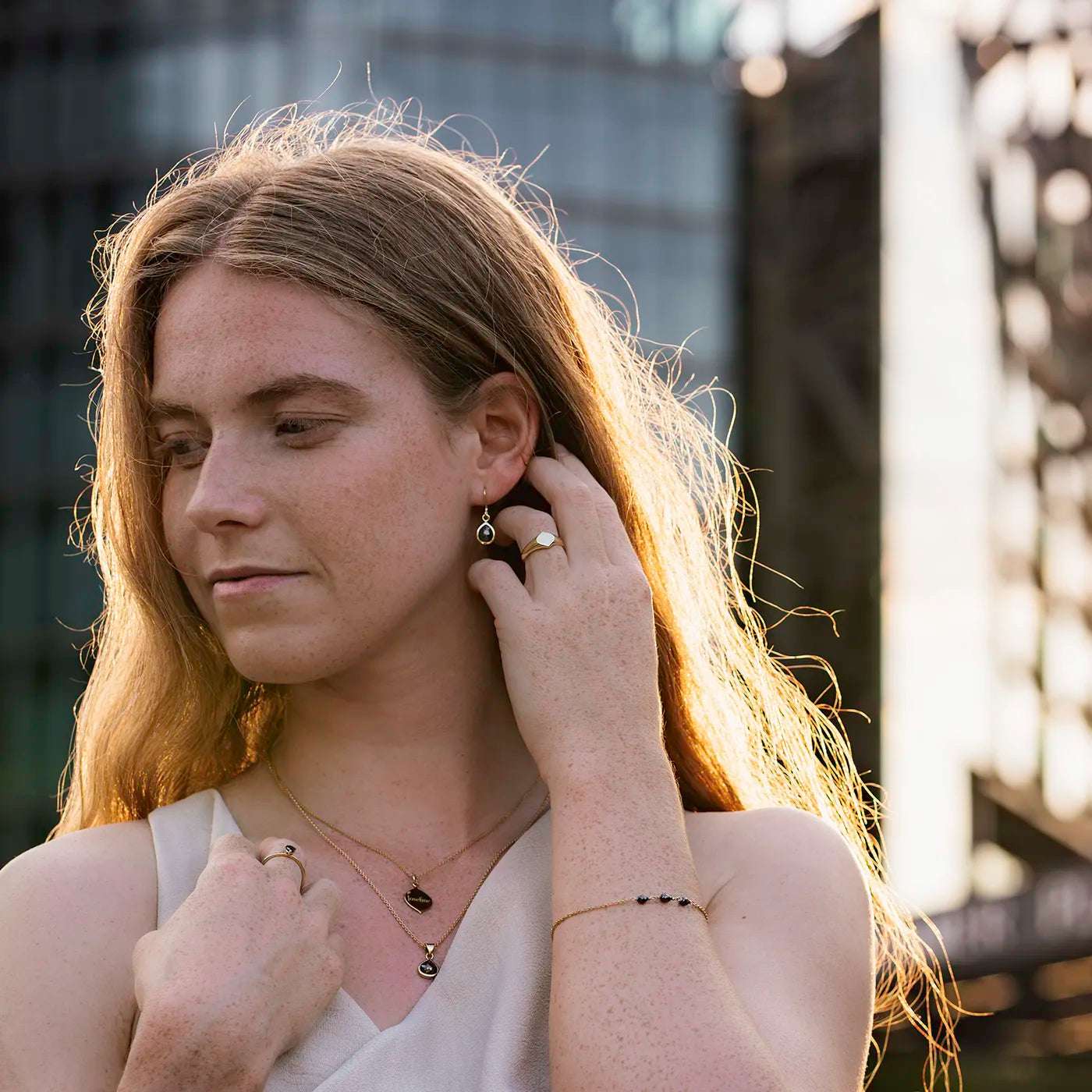 Siegelring Damen Gelbgold mit grosser Flaeche in Form Josefine Logo fuer Wunschgravur Frontansicht an Modelhand Ringfinger bei Sonnenuntergang Potsdamer Platz Hand hinter Ohr halbnah