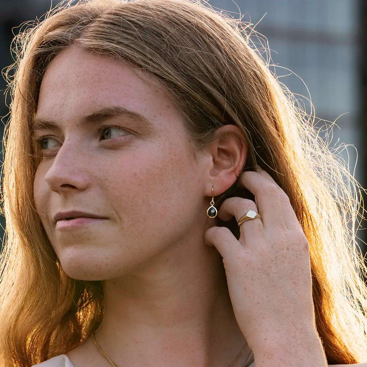 Siegelring Damen Gelbgold mit grosser Flaeche in Form Josefine Logo fuer Wunschgravur Frontansicht an Modelhand Ringfinger bei Sonnenuntergang Potsdamer Platz Hand hinter Ohr Closeup