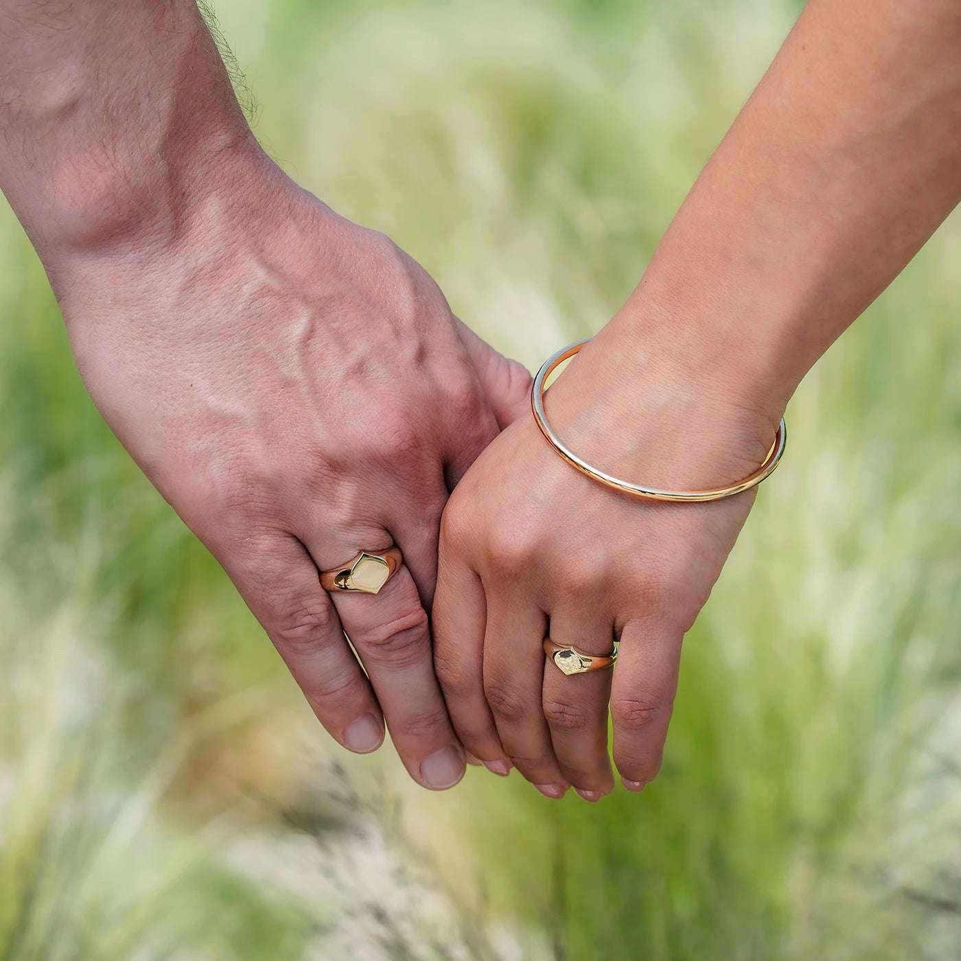 Siegelring Damen Gelbgold und Herrenring Platin mit grosser Flaeche in Form Josefine Logo fuer Wunschgravur Frontansicht an weiblich und maennlicher Modelhand Ringfingern halten Haende vor gruen halbnah