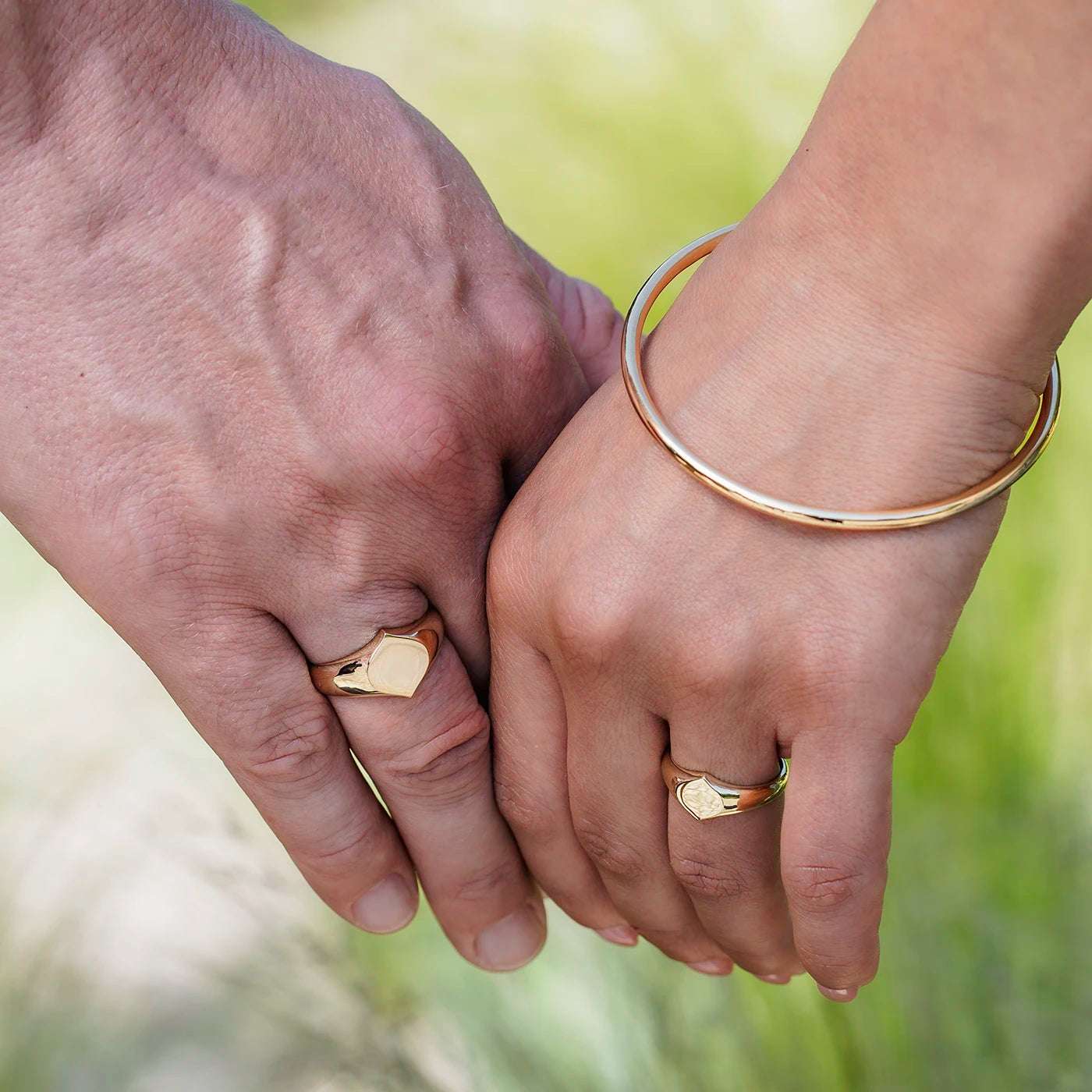 Siegelring Damen Gelbgold und Herrenring Platin mit grosser Flaeche in Form Josefine Logo fuer Wunschgravur Frontansicht an weiblich und maennlicher Modelhand Ringfingern halten Haende vor gruen closeup