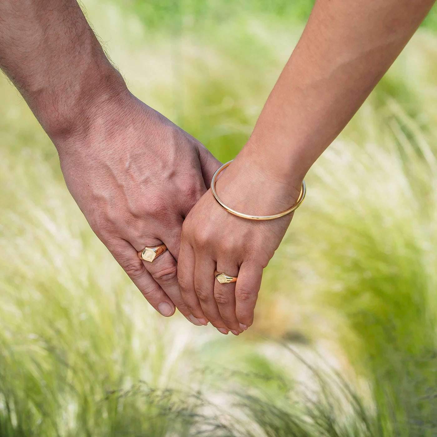 Siegelring Damen Gelbgold und Herrenring Platin mit grosser Flaeche in Form Josefine Logo fuer Wunschgravur Frontansicht an weiblich und maennlicher Modelhand Ringfingern halten Haende vor gruen