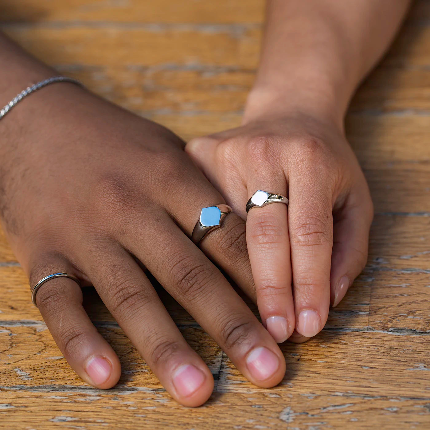 Siegelring Damen Herrenring Platin mit grosser Flaeche in Form Josefine Logo fuer Wunschgravur an weiblich und maennlicher Modelhand MIttel und Zeigefinger Haende uebereinander gelegt auf Tisch