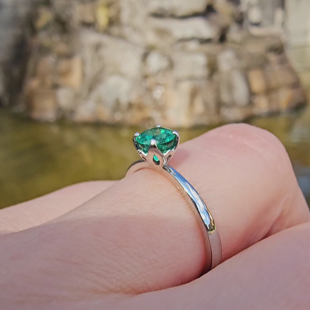 Petite Fleur Solitär Ring aus 950er Platin mit grünem Smaragd am Finger getragen vor Brunnen in Berlin Wilmersdorf