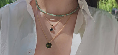 Frau trägt drei Gelbgold-Ketten im Layering, Smaragd-Edelsteinkette, Gravurkette Berlin Forever und Anhänger mit schwarzem Diamant-Tropfen 1,5 ct, handgefertigt in Berlin